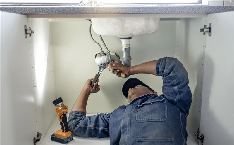 Plumber repairing pipes beneath a bathroom sink in Fayetteville