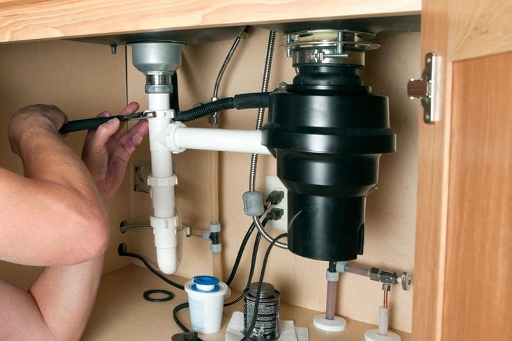Plumber installing a garbage disposal beneath a kitchen sink in Fayetteville