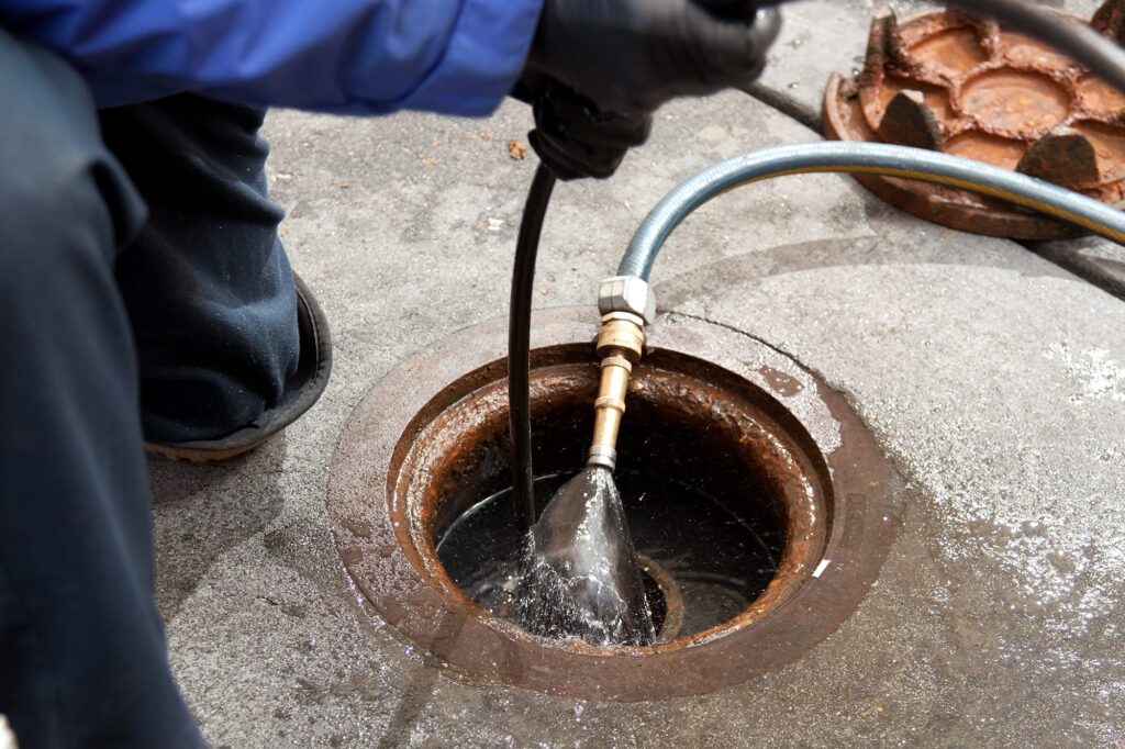 Plumber hydro jetting a sewer line through a manhole in Fayetteville