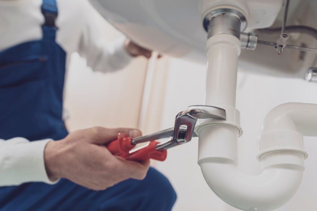 Plumber repairing a white drain pipe beneath a sink in Fayetteville