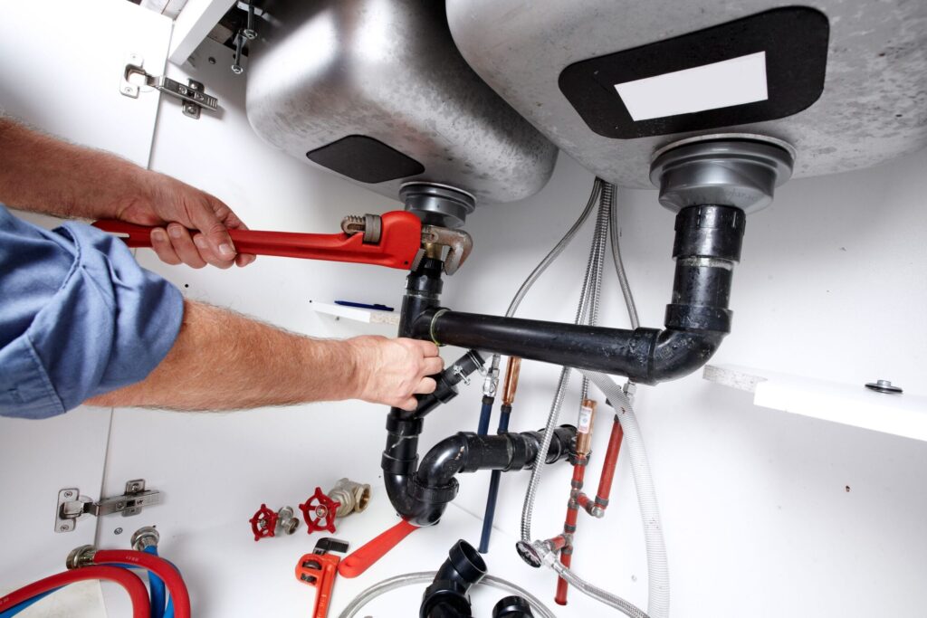 Plumber repairing drain pipes beneath a kitchen sink in Fayetteville